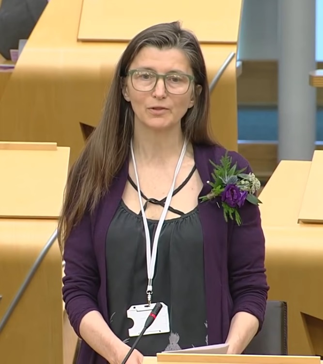 Scottish politician Ariane Burgess stands at a podium in parliament.