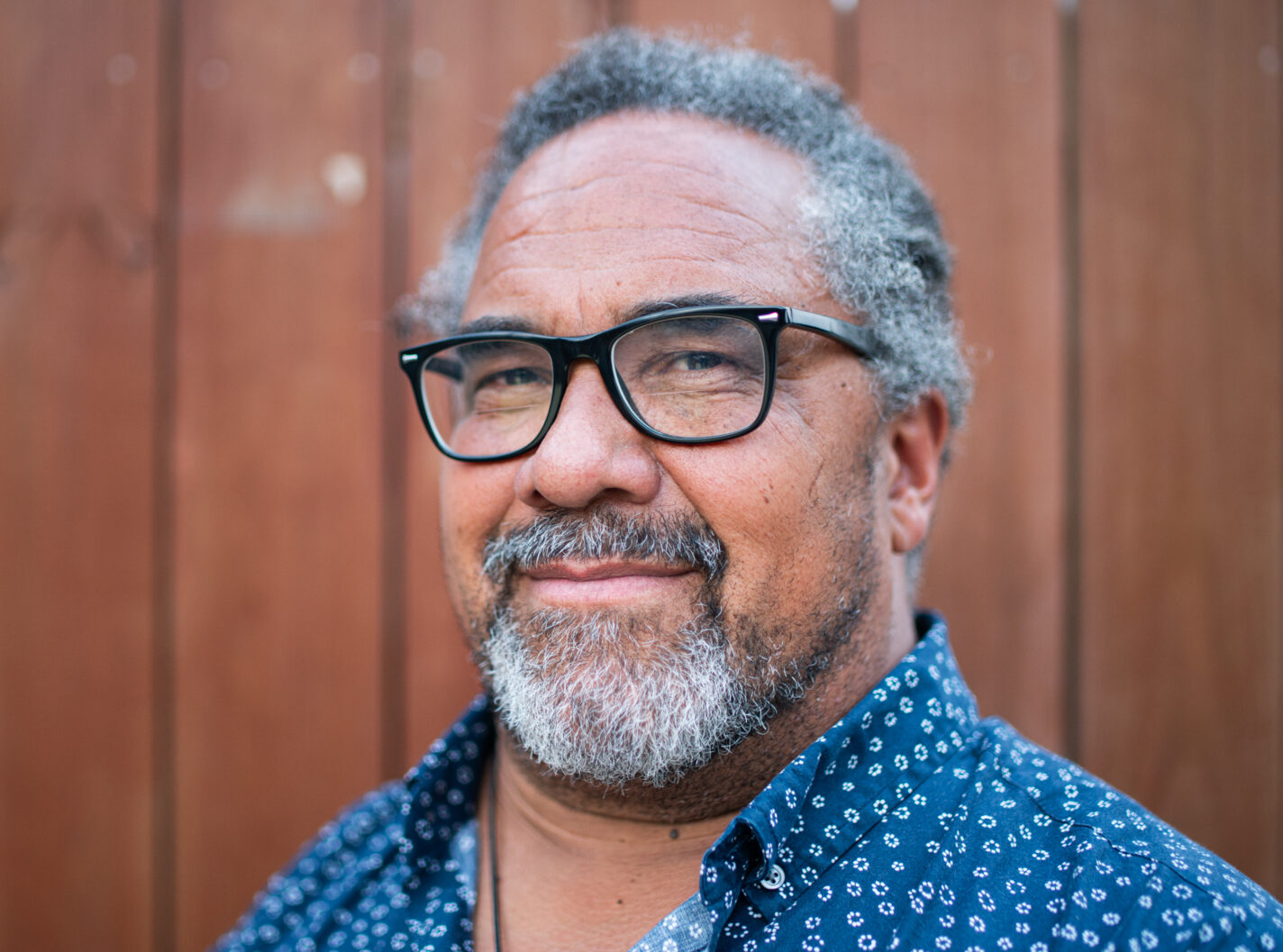 Fisherman and NAMA board member Jason Jarvis is smiling in front of a wooden paneled background. He is wearing black framed glasses and a blue button down shirt.
