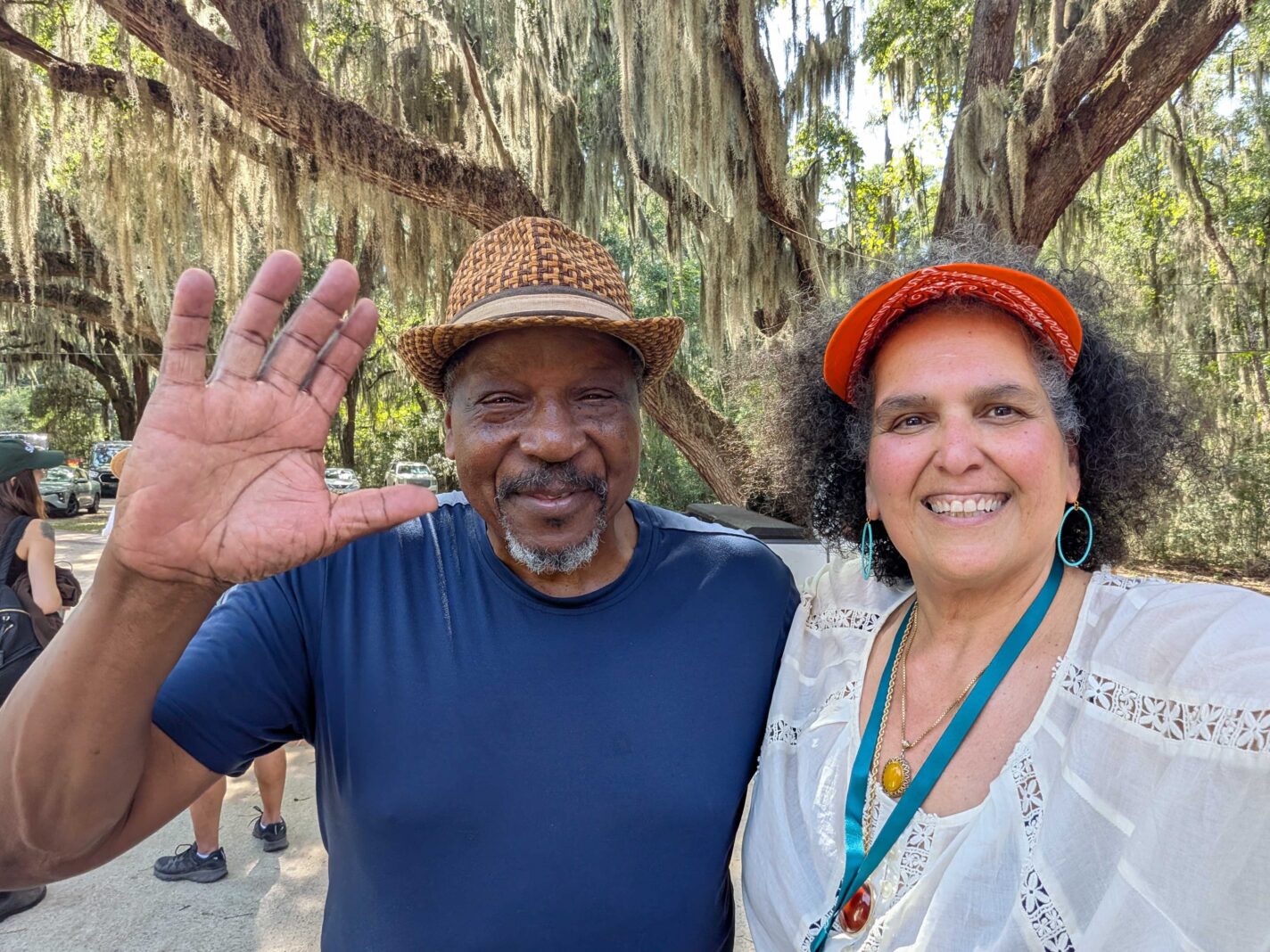 Captain Charles Abner and Niaz Dorry share a smile in front of a live oak tree in Savannah, GA. Niaz is wearing a white blouse and orange visor. Captain Charlie wears a brown fedors. The tree is covered in Spanish moss.
