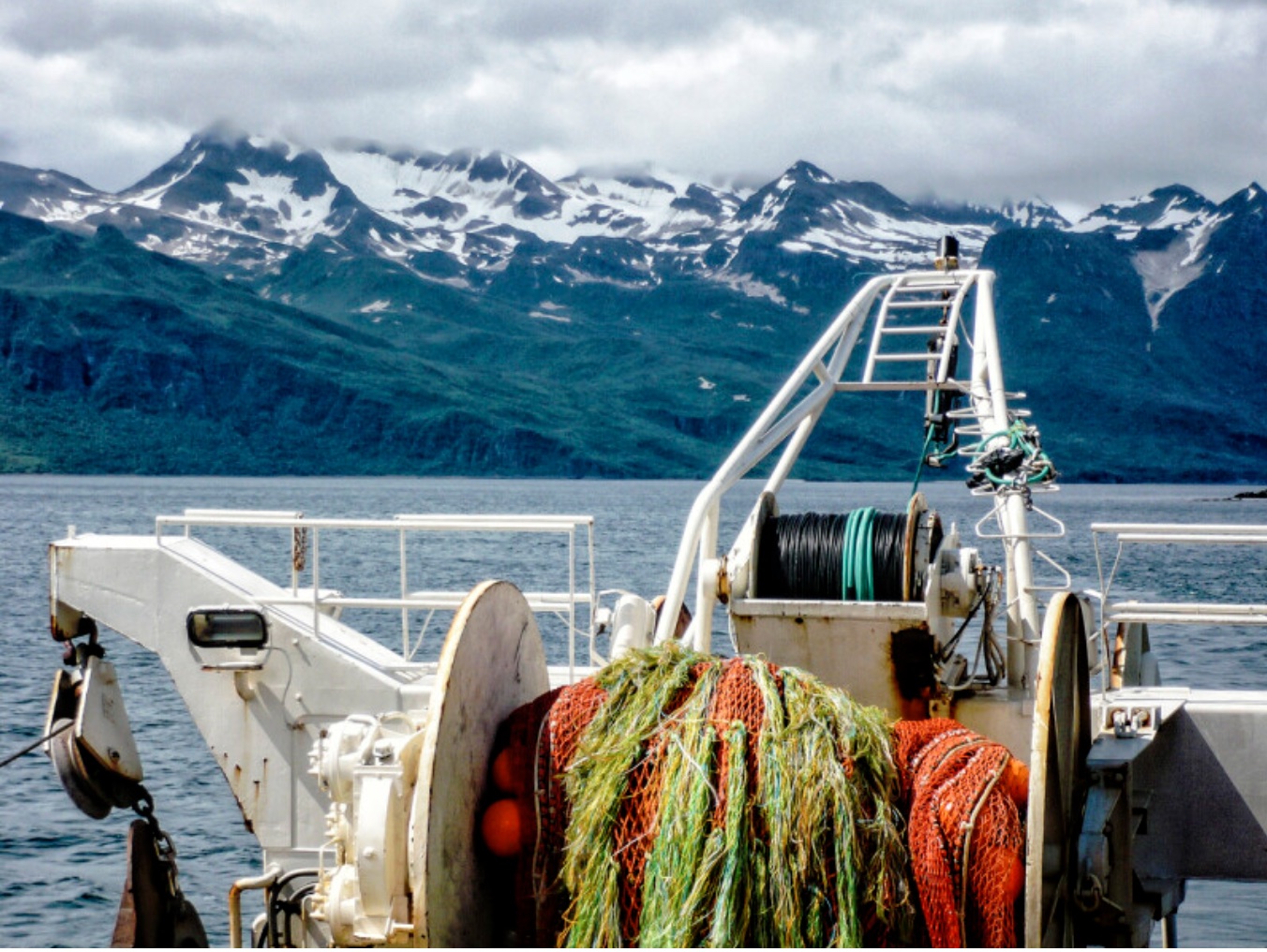 Fishing vessel equipment and colorful nets in coastal waters with snow-capped mountains in the background