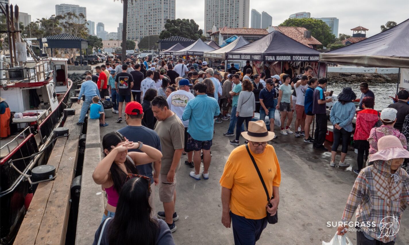 A crowded Saturday morning at the Tuna Harbor Dockside Market in San Diego. Palm trees and skyscrapers can be seen the background.